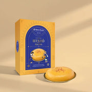 A yellow and blue box of  Classic Halwa next to a round golden halwa on a small plate, set against a warm beige background with soft shadows.