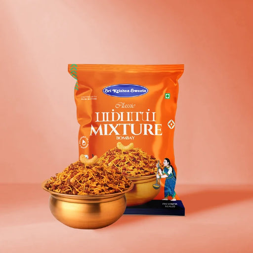 A bag of Sri Krishna Swasthya Classic Masala Mixture Bombay in orange packaging, displayed with two gold bowls filled with the spice mixture in front of it, set against a solid peach-pink background.