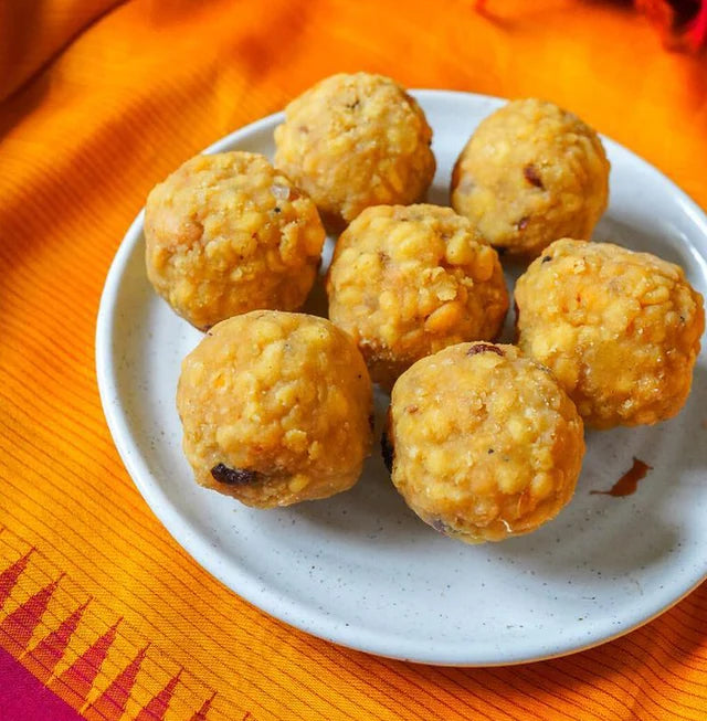 Six golden-brown fried sweet balls, likely laddoos or similar Indian sweets, arranged on a small white plate over a bright orange patterned fabric background.