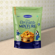 A stand-up pouch of Sri Krishnan Swetha Classic Cornflakes Mixture, featuring a light green body, dark blue text and bottom panel, and an illustration of a golden bowl of mixed cornflakes with two cartoon figures. The pouch is photographed against a beige textured background with a subtle repeating diamond pattern.