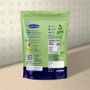 A stand-up pouch of Sit Kshitar Sweets back view, featuring a light green upper half and a dark blue lower half, with illustrations and product details printed on it, set against a patterned beige background.