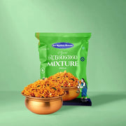 A green bag of Sri Krishnan Swetha Kerala Vellalai Mixture (Puzhai) is shown with two copper bowls filled with the orange-red spicy snack mixture in front of it, set against a solid light green background.