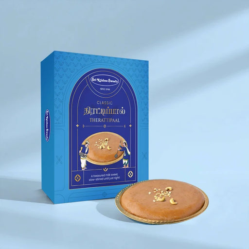 A blue boxed dessert product labeled 'Classic Therattipaal' stands next to a round golden-brown baked good on a small gold plate, photographed on a clean light blue studio background.